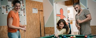 Zwei Frauen und ein Mann spielen Billard.
