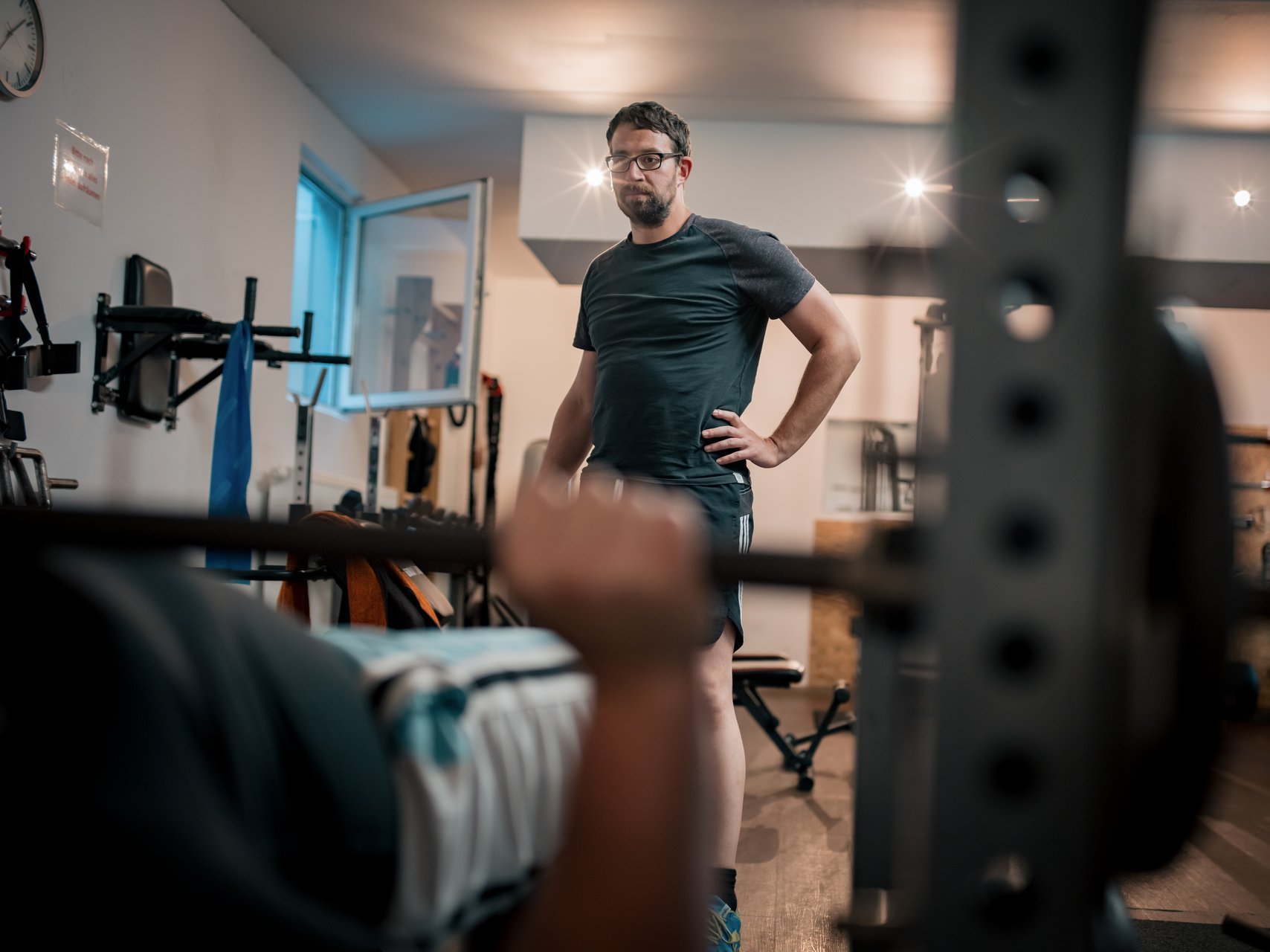 Ein Mann steht vor einer Hantelbank und beobachtet einen anderen Mann beim Training.