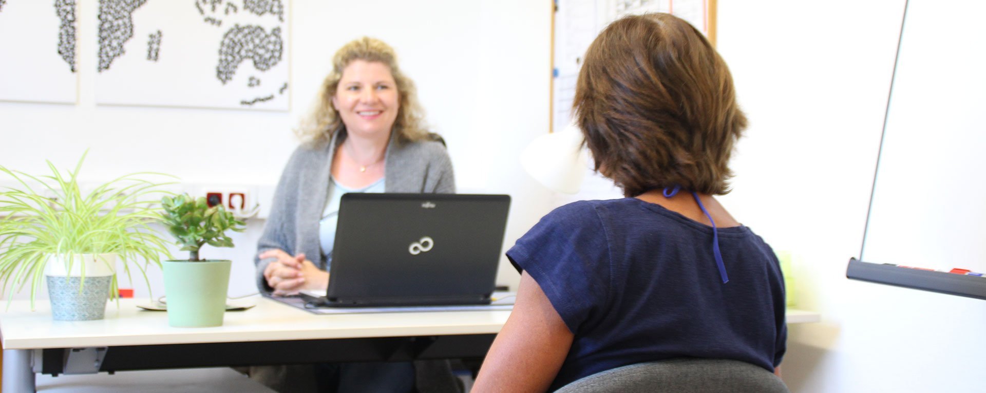 Besprechung im Büro: eine Frau am Schreibtisch mit Laptop hört einer anderen, ihr gegenüber sitzenden Frau zu