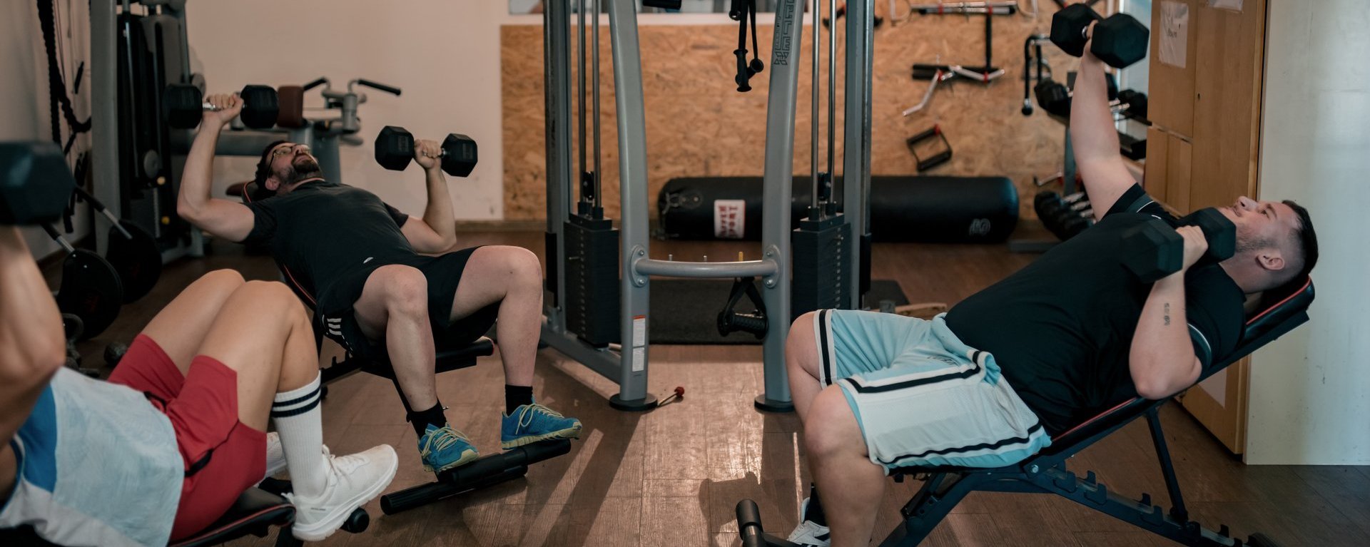 Drei Männer im Fitnessraum beim Hanteltraining.