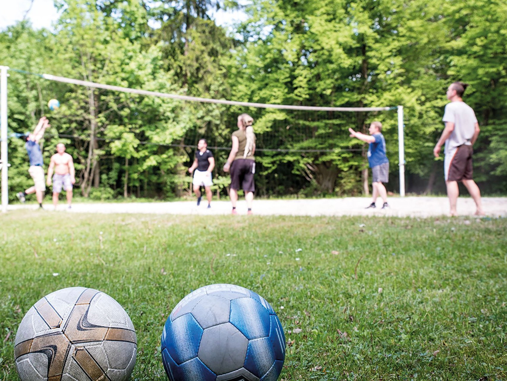 Nahaufnahme: Volleyball im Sand - dahinter das Netz und die Spieler/innen